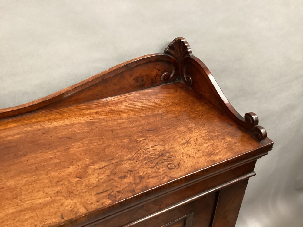 A Regency period side cabinet crafted from figured pollard oak featuring two panelled doors, a carved anthemion upstand, and a plinth base. View XVII