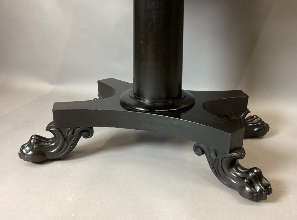 A George IV period ebonised centre table featuring a white rectangular marble top set above a shaped apron, central column pedestal, and quadform base with carved paw feet. View III