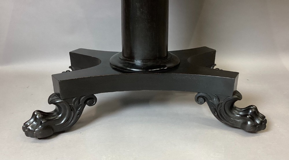 A George IV period ebonised centre table featuring a white rectangular marble top set above a shaped apron, central column pedestal, and quadform base with carved paw feet. View XII