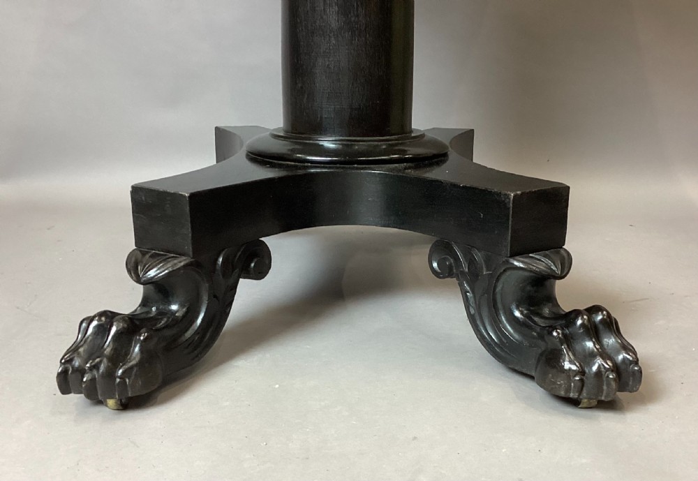 A George IV period ebonised centre table featuring a white rectangular marble top set above a shaped apron, central column pedestal, and quadform base with carved paw feet. View XIII