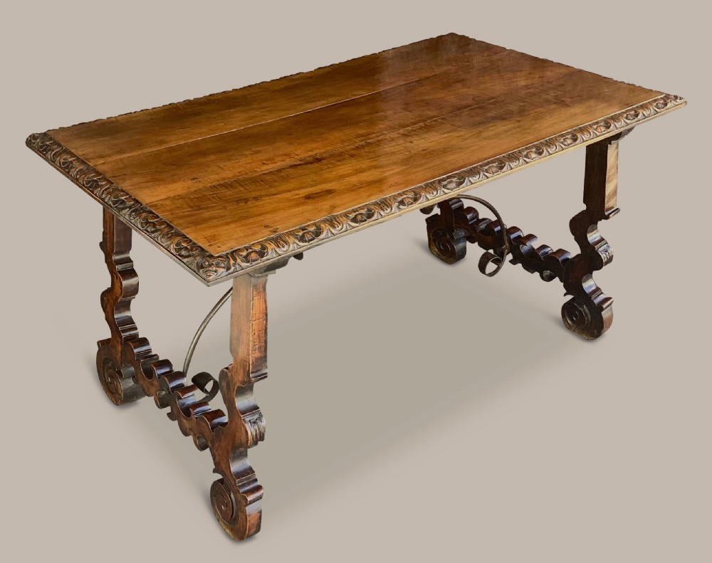 An 18th-century Spanish walnut and fruitwood centre table featuring carved trestle supports, decorative edge moulding, and wrought iron stretchers.