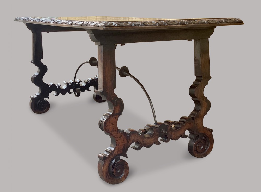An 18th-century Spanish walnut and fruitwood centre table featuring carved trestle supports, decorative edge moulding, and wrought iron stretchers. View V