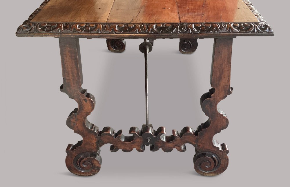 An 18th-century Spanish walnut and fruitwood centre table featuring carved trestle supports, decorative edge moulding, and wrought iron stretchers. View IX