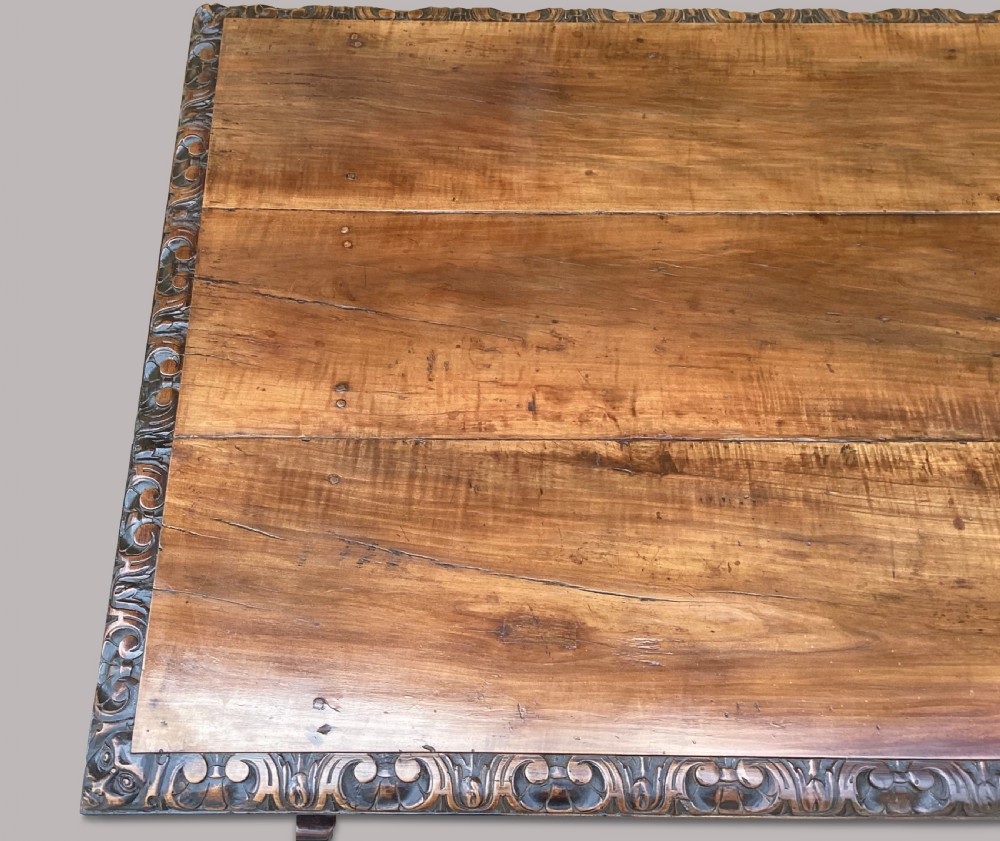 An 18th-century Spanish walnut and fruitwood centre table featuring carved trestle supports, decorative edge moulding, and wrought iron stretchers. View X