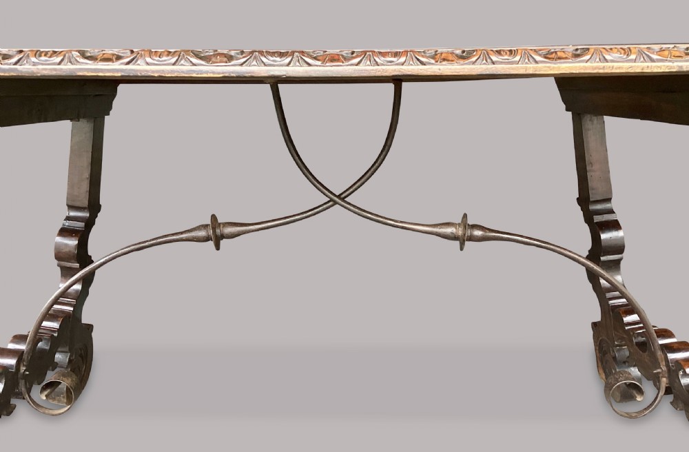 An 18th-century Spanish walnut and fruitwood centre table featuring carved trestle supports, decorative edge moulding, and wrought iron stretchers. View XVII