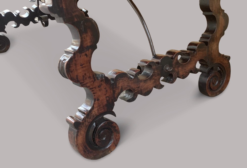 An 18th-century Spanish walnut and fruitwood centre table featuring carved trestle supports, decorative edge moulding, and wrought iron stretchers. View XX