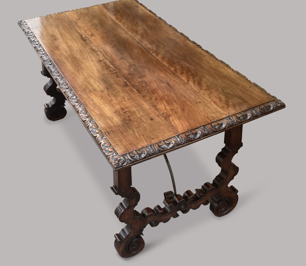 An 18th-century Spanish walnut and fruitwood centre table featuring carved trestle supports, decorative edge moulding, and wrought iron stretchers. View XXI