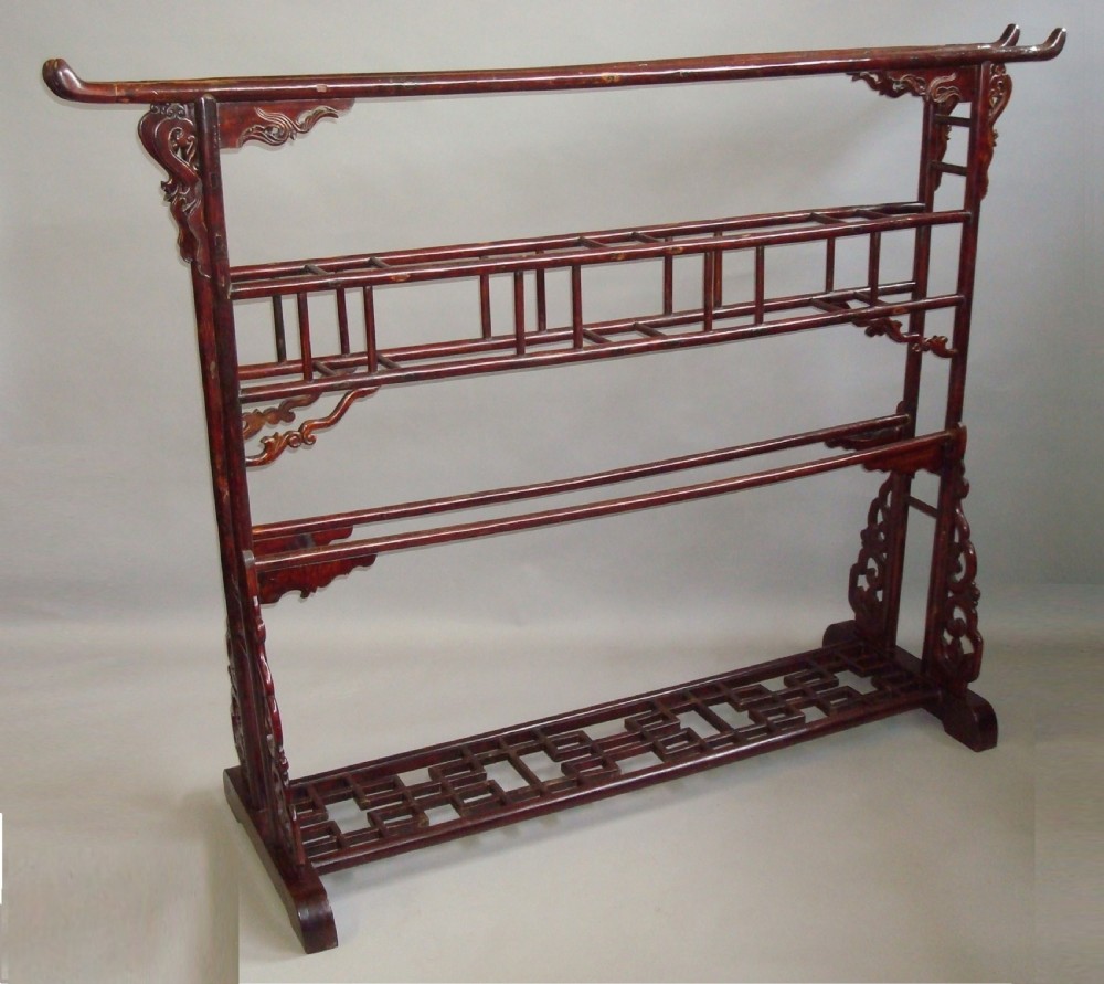 A large nineteenth-century Chinese dark red lacquered wooden robe stand featuring extended top rails, carved decorative spandrels, and a lattice bottom base.
