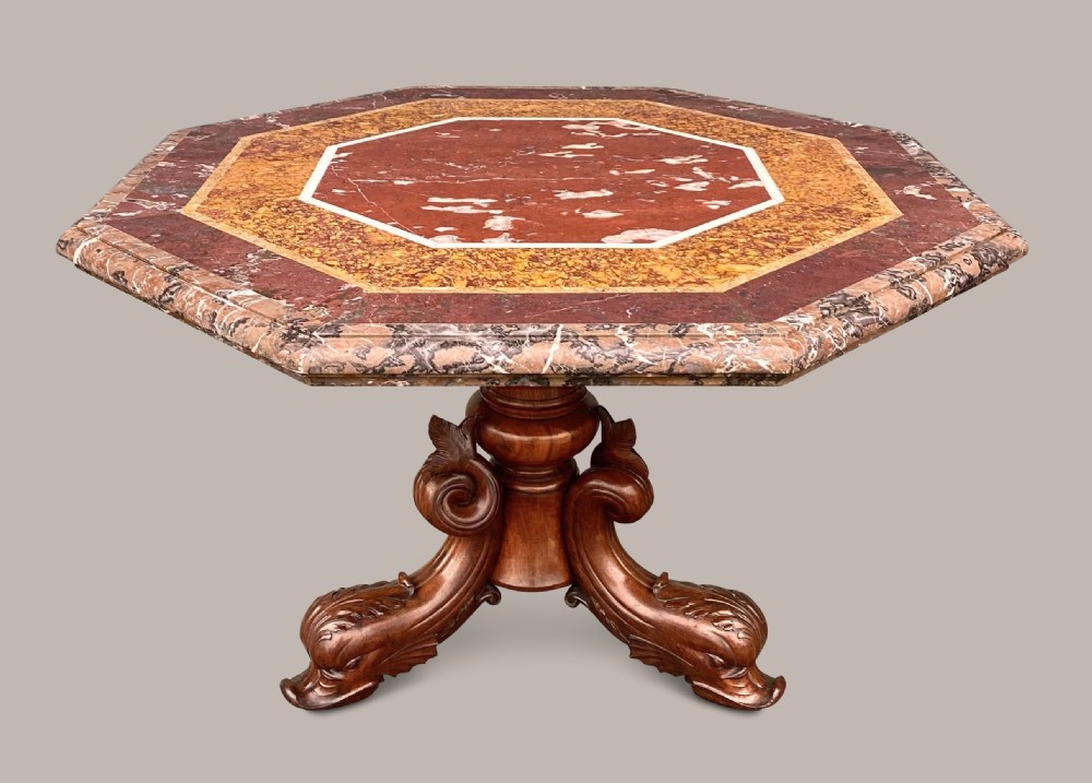 An octagonal 19th-century centre table with a geometric inlaid specimen marble top supported on a carved walnut pedestal base with scroll feet.