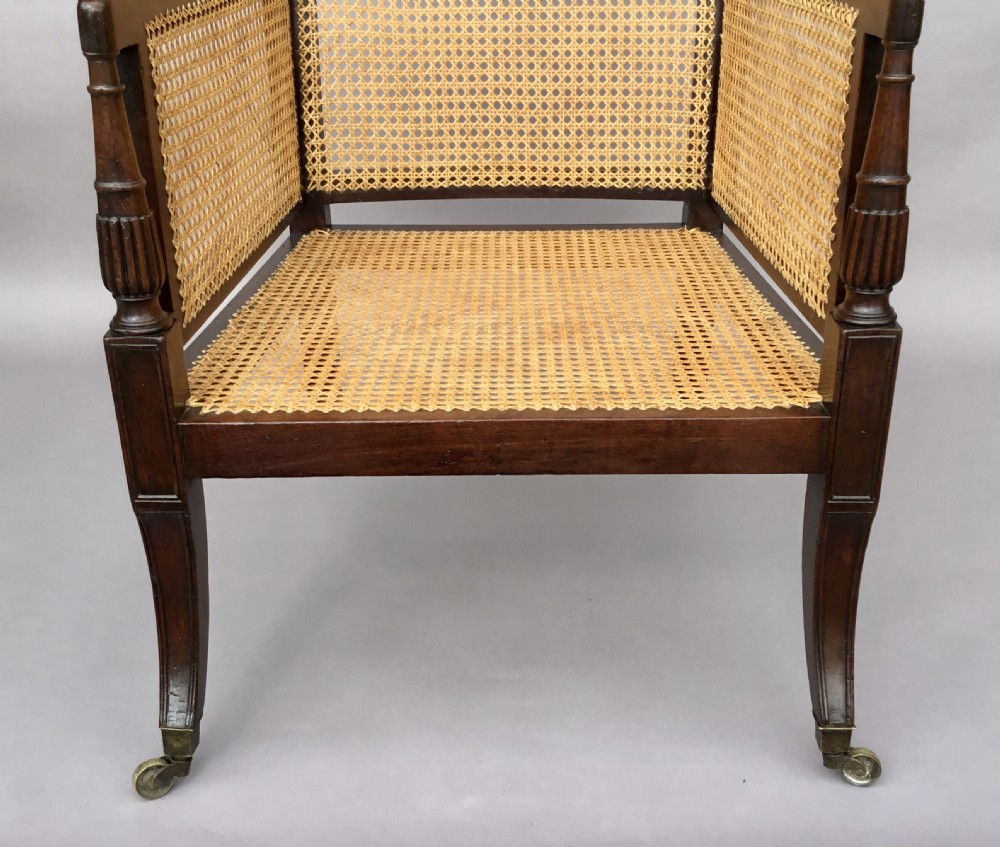 A Regency mahogany bergere library chair with woven cane back, sides, and seat, set on curved legs with brass castors. View IV