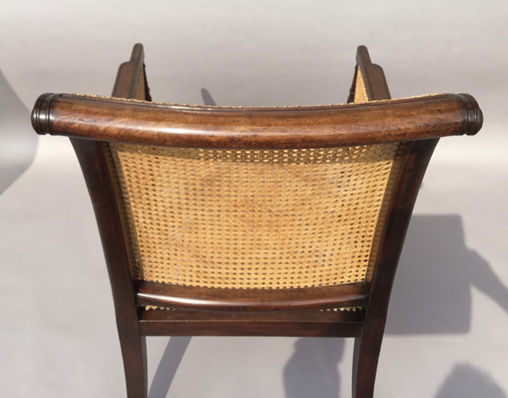 A Regency mahogany bergere library chair with woven cane back, sides, and seat, set on curved legs with brass castors. View VI