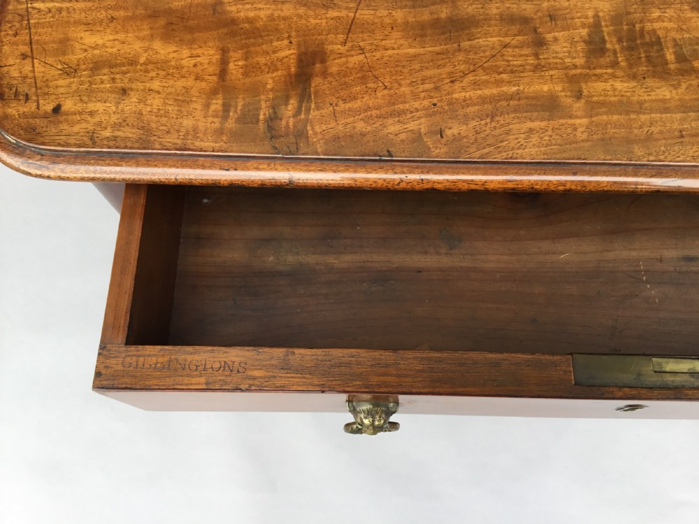 An Irish Regency mahogany centre table with two frieze drawers and brass lion mask handles, resting on end trestle supports with sabre legs and brass castors. View V