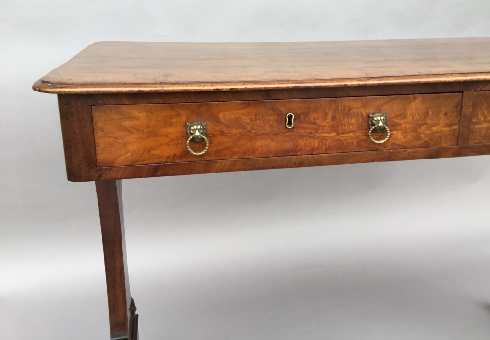 An Irish Regency mahogany centre table with two frieze drawers and brass lion mask handles, resting on end trestle supports with sabre legs and brass castors. View XV