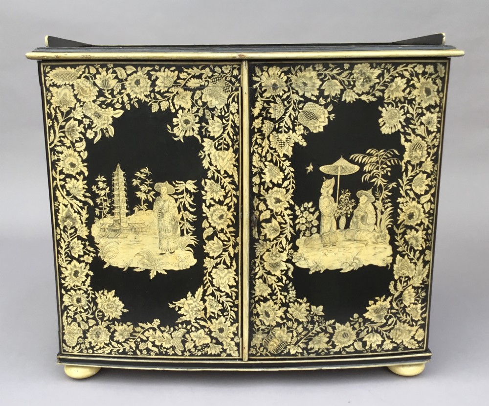 A Regency black lacquered collectors cabinet on stand featuring detailed cream and gilt Chinoiserie penwork illustrations of oriental figures and floral borders. View VI