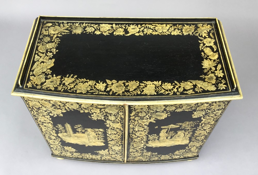 A Regency black lacquered collectors cabinet on stand featuring detailed cream and gilt Chinoiserie penwork illustrations of oriental figures and floral borders. View XI
