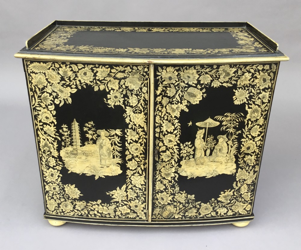A Regency black lacquered collectors cabinet on stand featuring detailed cream and gilt Chinoiserie penwork illustrations of oriental figures and floral borders. View XIV