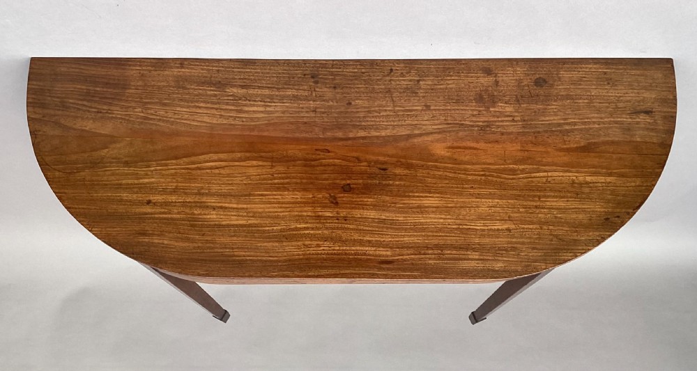 A George III mahogany demilune console table featuring a semi-circular top, plain apron, and four long square tapered legs. View II