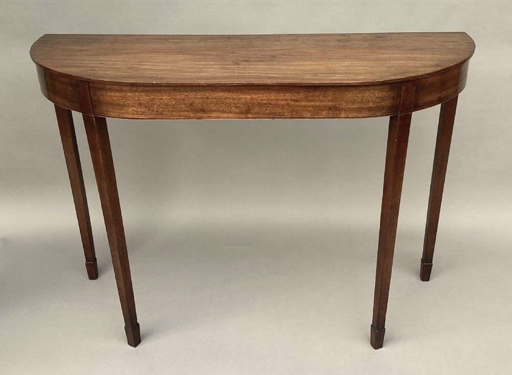 A George III mahogany demilune console table featuring a semi-circular top, plain apron, and four long square tapered legs. View VIII