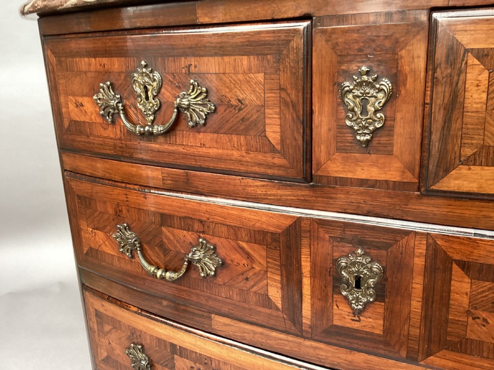 An 18th-century Louis XV bow-fronted kingwood commode featuring geometric parquetry drawers, cast bronze handles, keyhole escutcheons, and a thick marble top. View XII