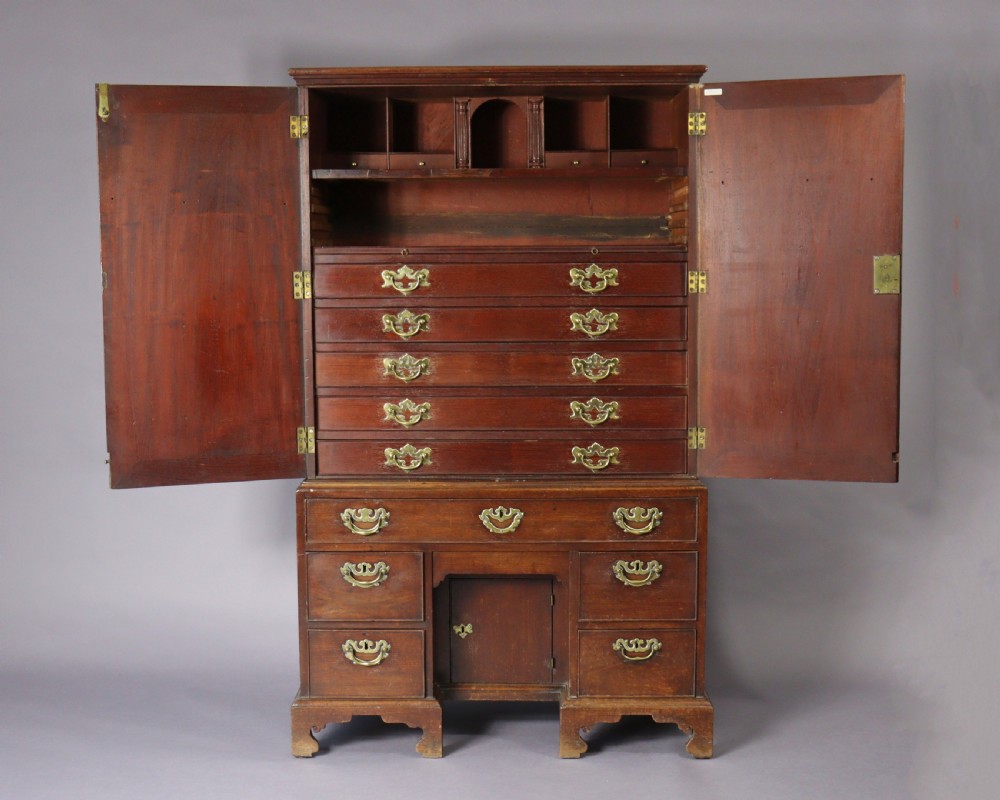 An eighteenth-century George II red walnut cabinet on a kneehole base with open doors revealing fitted internal drawers and pigeonholes above brass-handled drawers.
