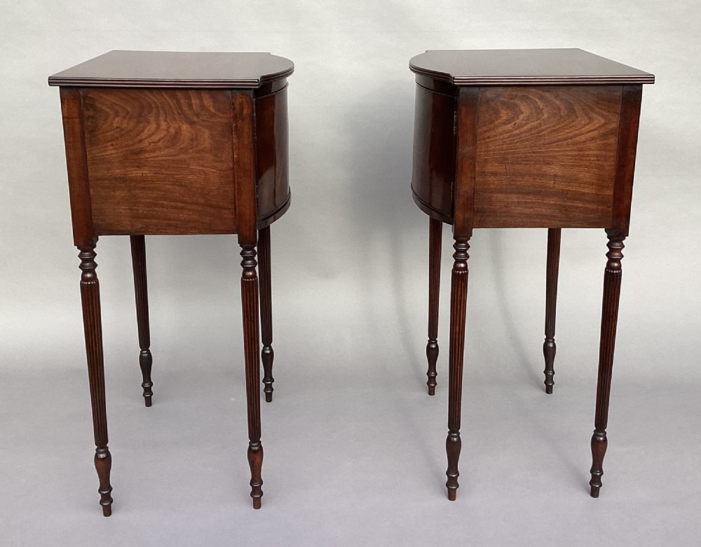 A matching pair of George III mahogany bowfront bedside cabinets standing on slender reeded turned legs with single cupboard doors. View VI