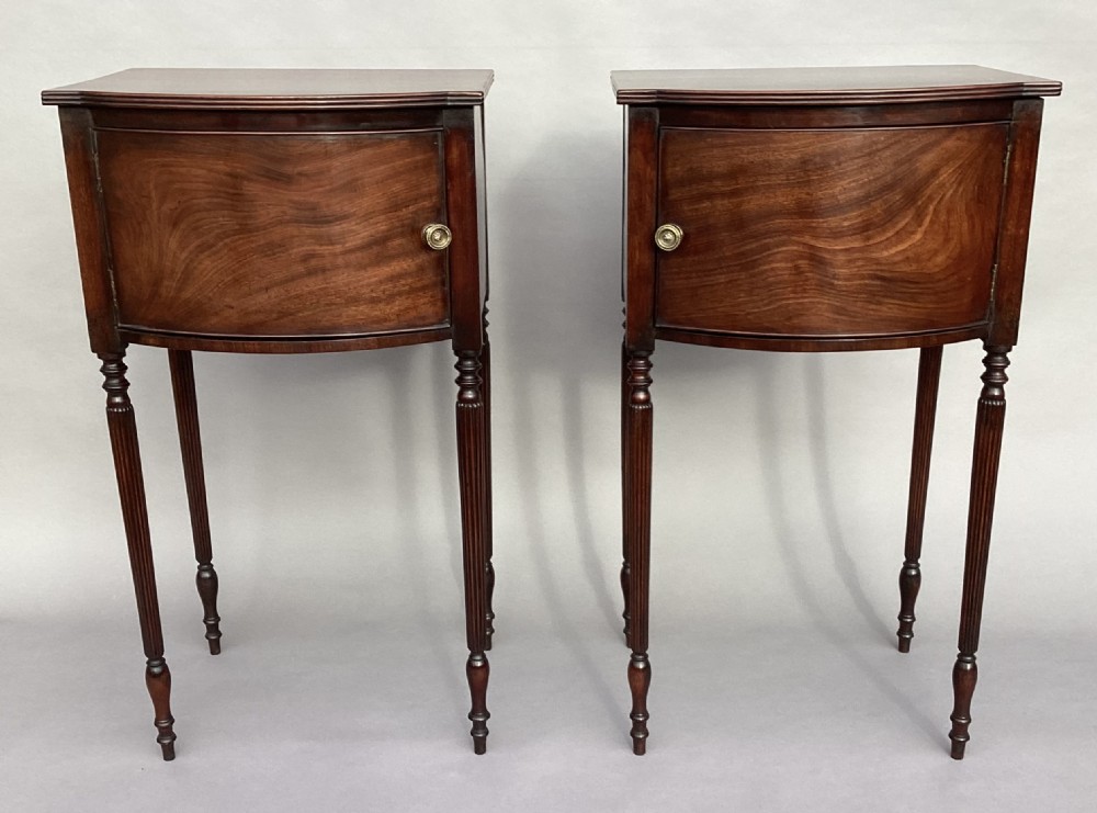 A matching pair of George III mahogany bowfront bedside cabinets standing on slender reeded turned legs with single cupboard doors. View VII
