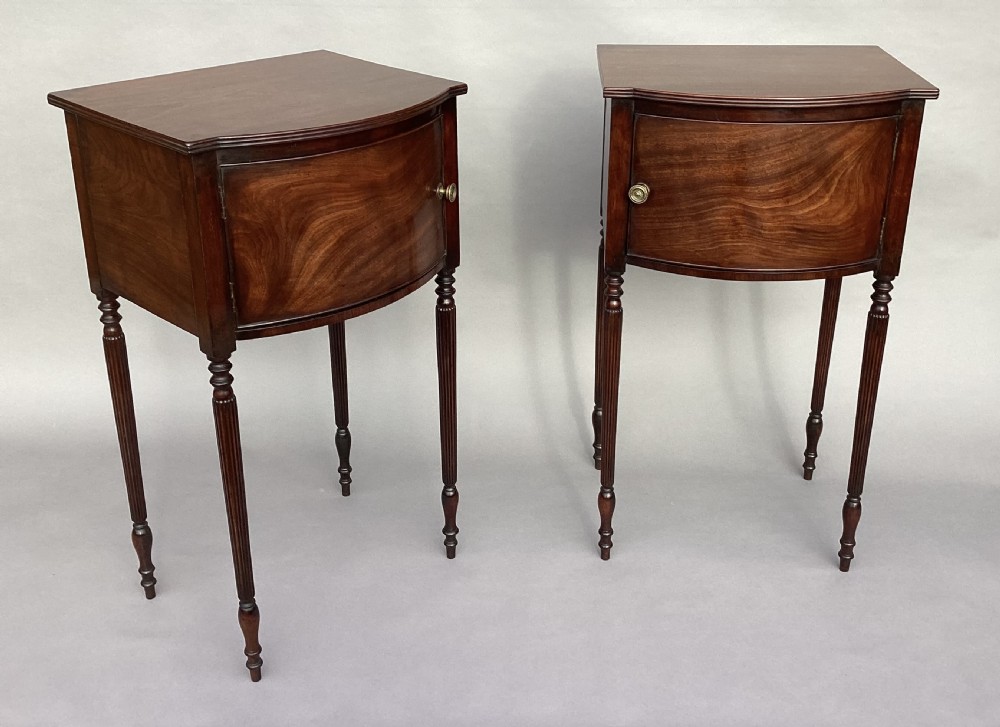 A matching pair of George III mahogany bowfront bedside cabinets standing on slender reeded turned legs with single cupboard doors. View VIII
