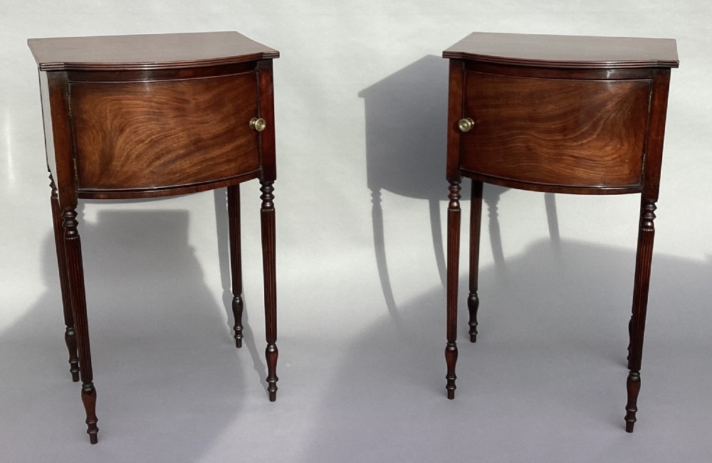 A matching pair of George III mahogany bowfront bedside cabinets standing on slender reeded turned legs with single cupboard doors. View IX