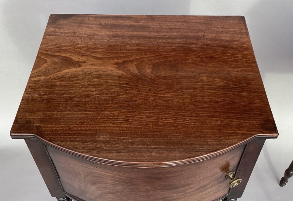 A matching pair of George III mahogany bowfront bedside cabinets standing on slender reeded turned legs with single cupboard doors. View XV