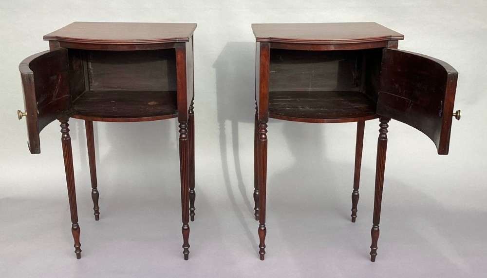 A matching pair of George III mahogany bowfront bedside cabinets standing on slender reeded turned legs with single cupboard doors. View XVIII