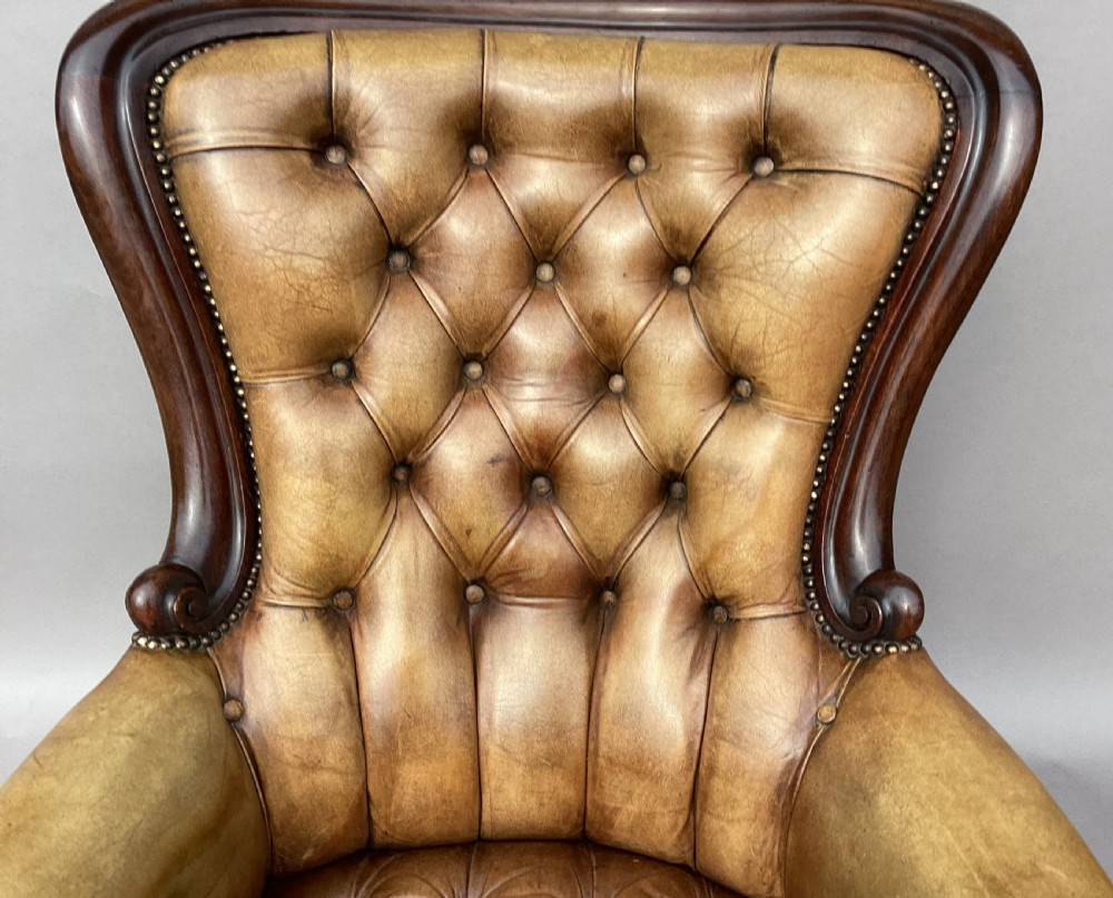 A mid-19th-century Victorian mahogany library armchair featuring button-tufted tan leather upholstery, brass stud trim, carved cabriole front legs, and brass castors. View IX
