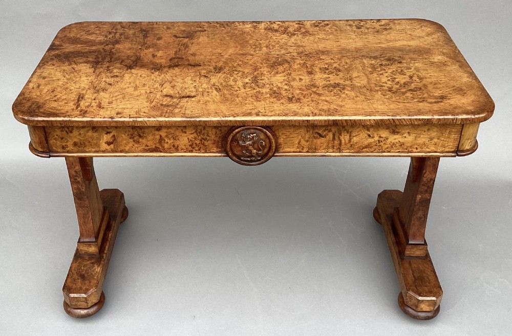 A mid-19th-century centre table crafted from figured burr and pollard oak, featuring rounded corners, a central carved medallion on the frieze, and twin end-standard supports on sledge bases.