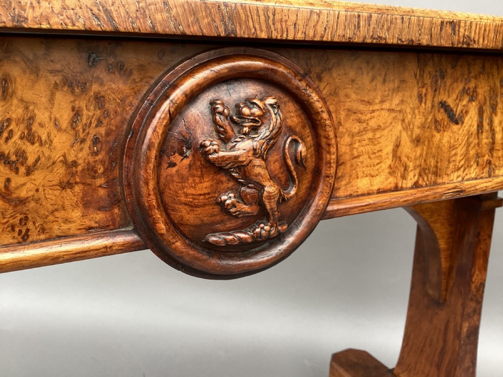 A mid-19th-century centre table crafted from figured burr and pollard oak, featuring rounded corners, a central carved medallion on the frieze, and twin end-standard supports on sledge bases. View IV
