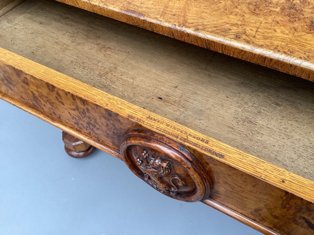 A mid-19th-century centre table crafted from figured burr and pollard oak, featuring rounded corners, a central carved medallion on the frieze, and twin end-standard supports on sledge bases. View VI