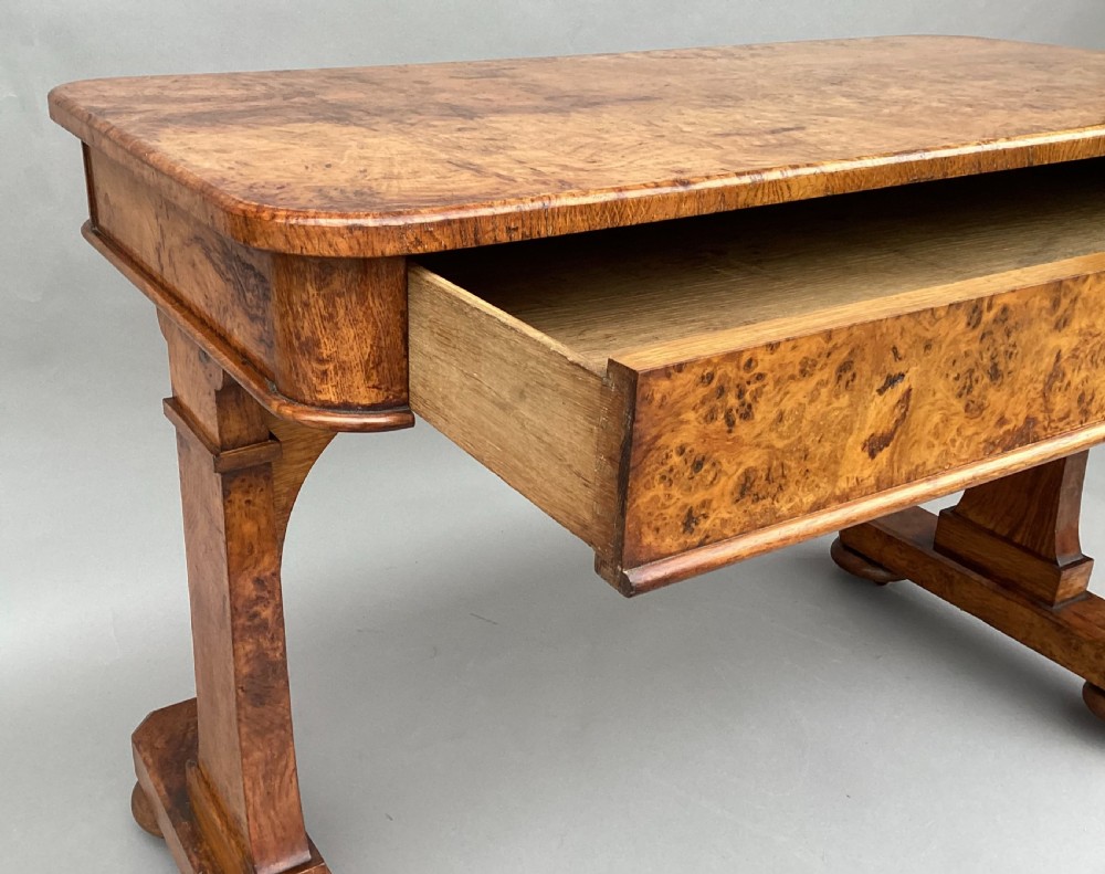 A mid-19th-century centre table crafted from figured burr and pollard oak, featuring rounded corners, a central carved medallion on the frieze, and twin end-standard supports on sledge bases. View XIV