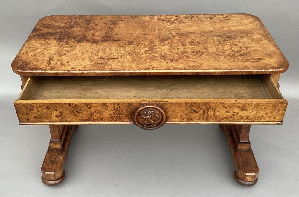 A mid-19th-century centre table crafted from figured burr and pollard oak, featuring rounded corners, a central carved medallion on the frieze, and twin end-standard supports on sledge bases. View XV