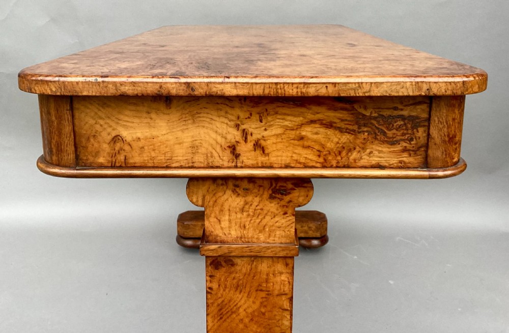 A mid-19th-century centre table crafted from figured burr and pollard oak, featuring rounded corners, a central carved medallion on the frieze, and twin end-standard supports on sledge bases. View XVI