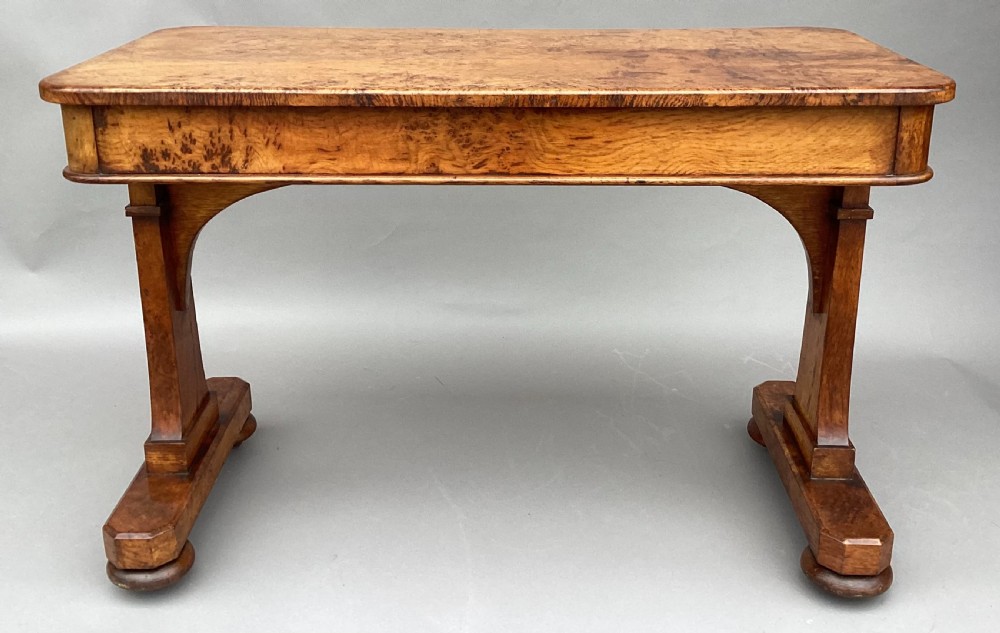 A mid-19th-century centre table crafted from figured burr and pollard oak, featuring rounded corners, a central carved medallion on the frieze, and twin end-standard supports on sledge bases. View XVII