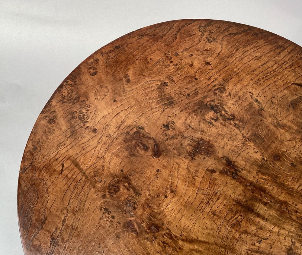 An 18th-century Irish Georgian burr oak tripod wine table featuring a circular top, turned central pedestal, and three cabriole legs terminating in pad feet. View X