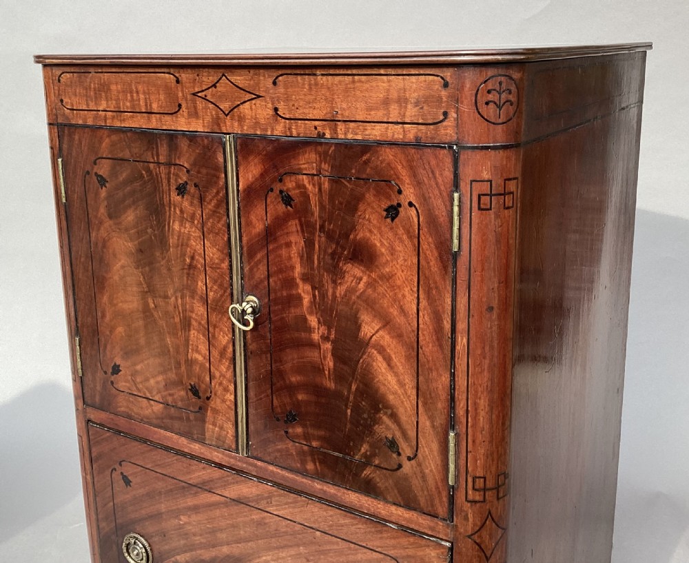 A Regency flame mahogany pedestal cabinet featuring dark ebony inlay stringing, upper double doors, a lower cupboard door, and brass paw feet. View V