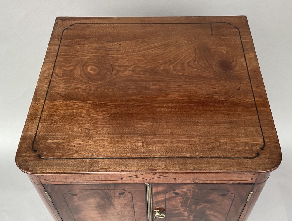 A Regency flame mahogany pedestal cabinet featuring dark ebony inlay stringing, upper double doors, a lower cupboard door, and brass paw feet. View VII