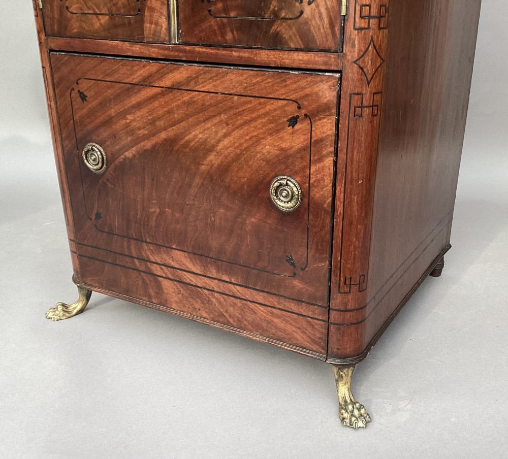 A Regency flame mahogany pedestal cabinet featuring dark ebony inlay stringing, upper double doors, a lower cupboard door, and brass paw feet. View VIII