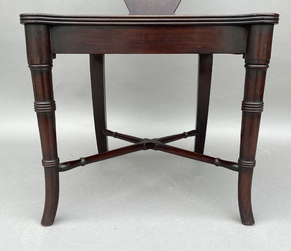 A pair of George III mahogany hall chairs with shield-shaped backs featuring circular brass inlays, dished wooden seats, and turned legs. View IX
