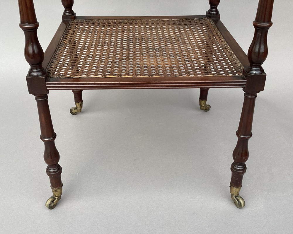 A four-tiered Regency mahogany whatnot stand featuring woven cane shelves, turned spindle supports, top finials, and brass castors. View VII