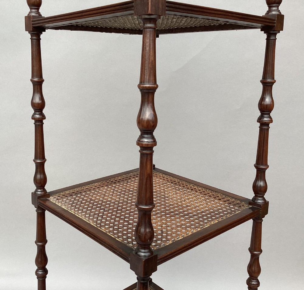 A four-tiered Regency mahogany whatnot stand featuring woven cane shelves, turned spindle supports, top finials, and brass castors. View VIII