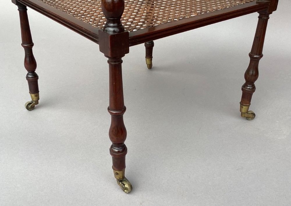A four-tiered Regency mahogany whatnot stand featuring woven cane shelves, turned spindle supports, top finials, and brass castors. View X