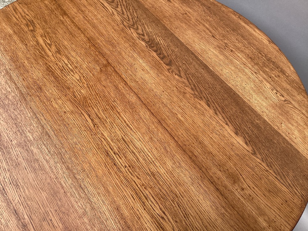 A circular 19th-century solid oak table with a warm brown grain finish, supported by a splayed base featuring dark iron strapwork. View IV