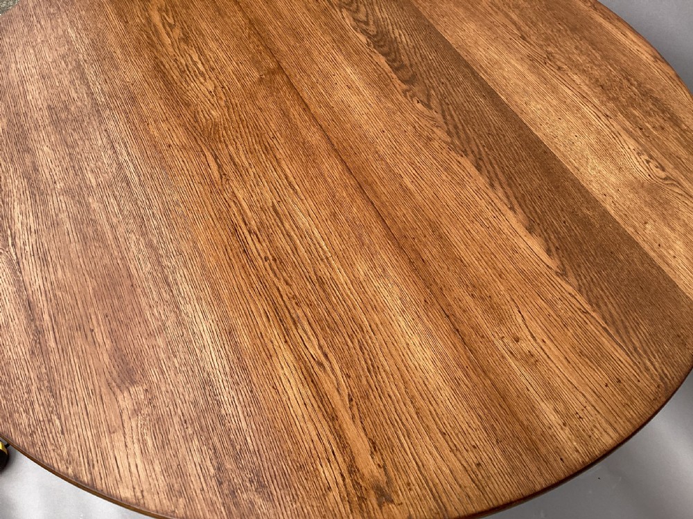 A circular 19th-century solid oak table with a warm brown grain finish, supported by a splayed base featuring dark iron strapwork. View VIII
