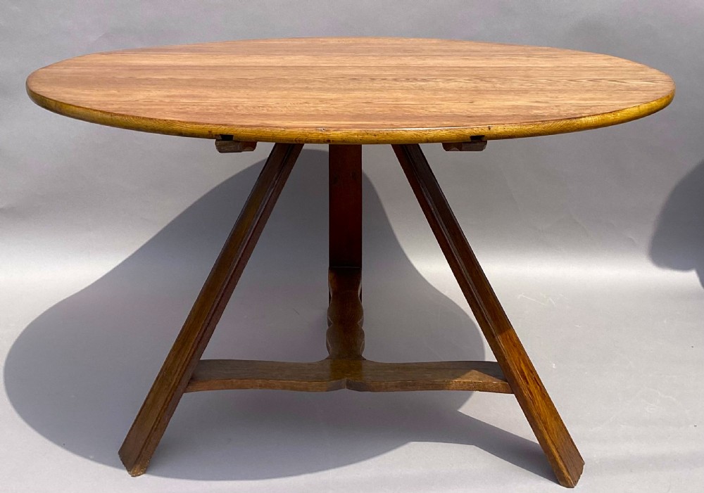 A circular 19th-century solid oak table with a warm brown grain finish, supported by a splayed base featuring dark iron strapwork. View X