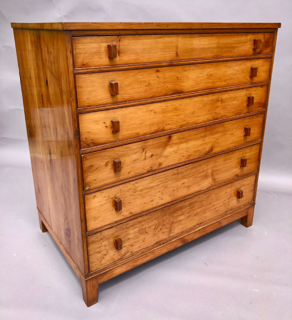 An Arts and Crafts solid yew wood chest featuring six graduated drawers with simple square wooden pulls.